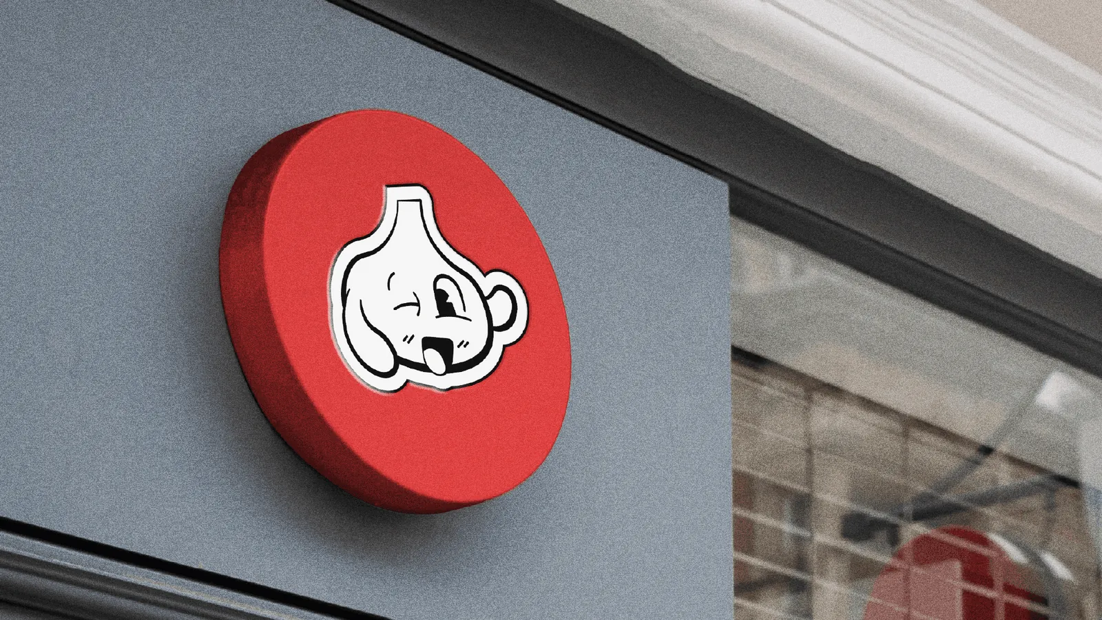 Placa redonda vermelha com o mascote de alho na fachada da Alho Burger